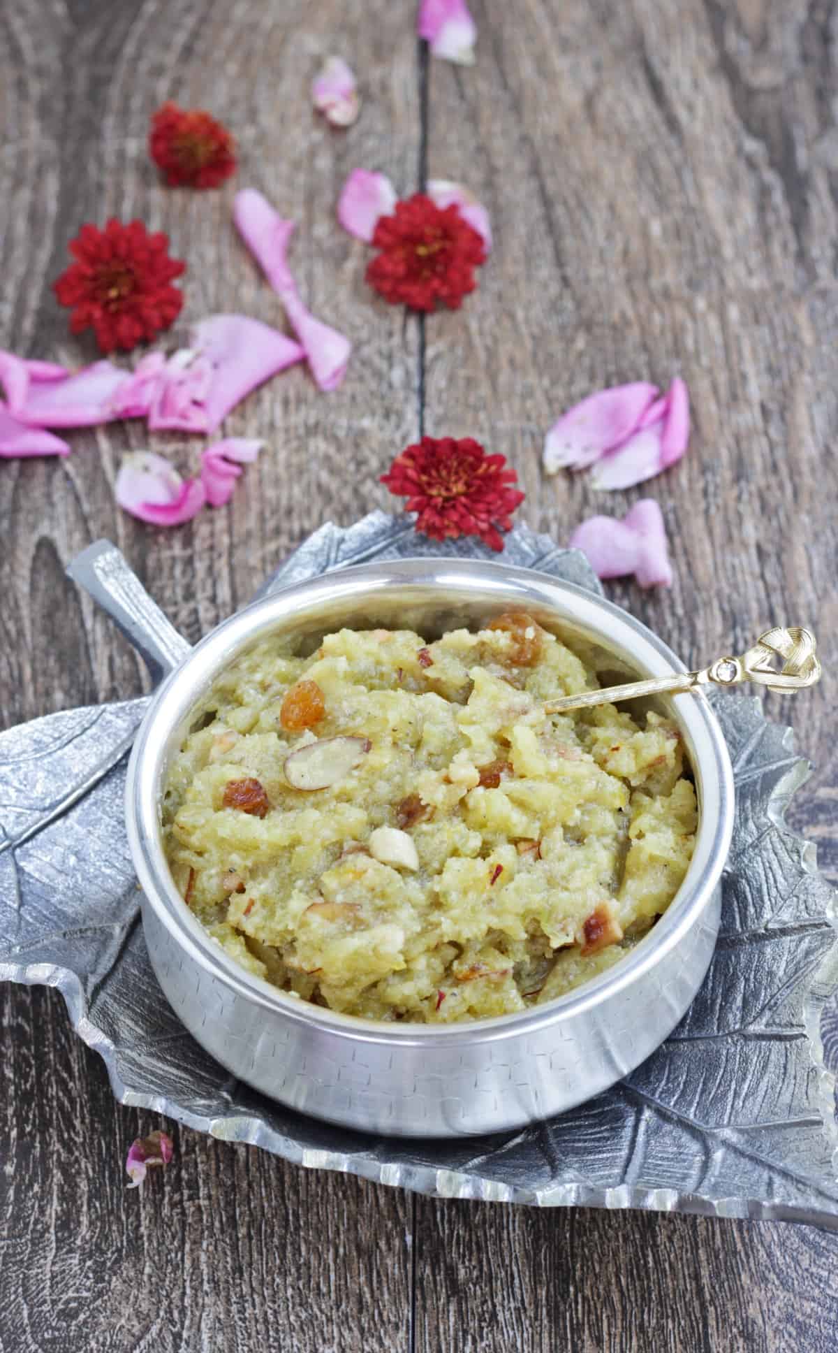 Bottle gourd halwa served in a silver bowl with spoon and flowers scattered around.