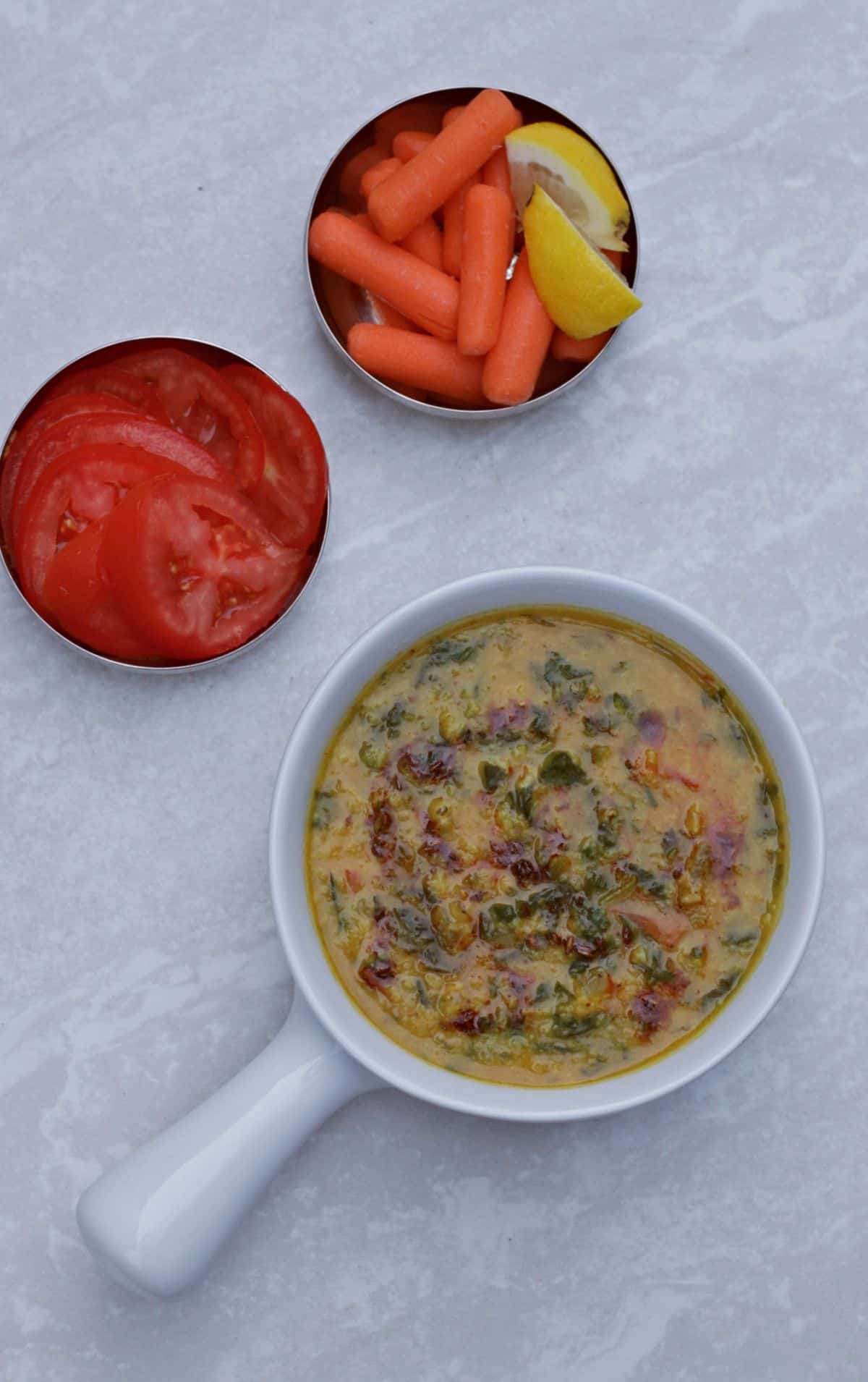 dal palak curry in a white bowl with carrot and tomatoes on the side
